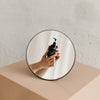 Circular mirror reflecting a pair of hands holding the Basic Maintenance Formula 09 Shave Gel bottle